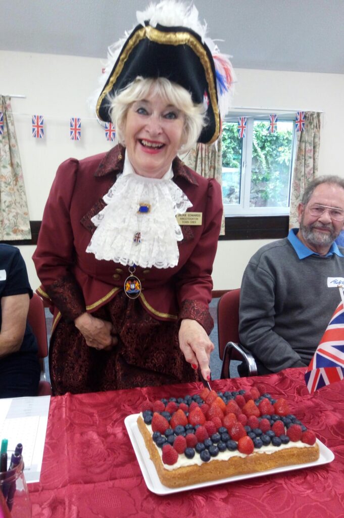 Kingsteignton Town Crier cutting a Union Jack cake decorated with raspberries, strawberries and blueberries